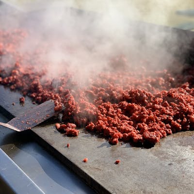 Close-up of sizzling ground beef cooking on hot grill with steam rising.