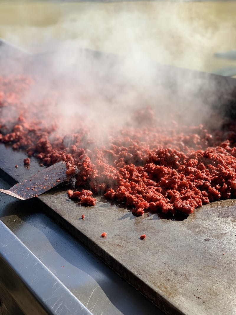 Close-up of sizzling ground beef cooking on hot grill with steam rising.