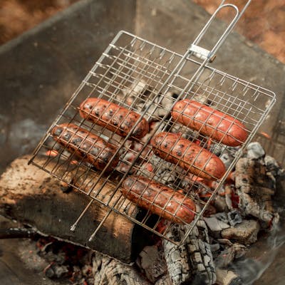 Sizzling sausages being grilled over a smoky outdoor fire for a barbecue.